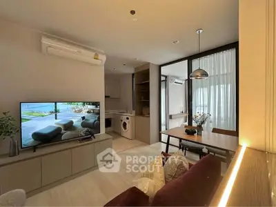 Modern living room with open kitchen and dining area, featuring sleek furniture and natural lighting.