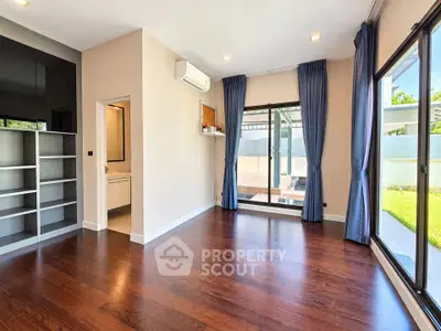 Spacious empty room with hardwood floors and large windows overlooking garden.