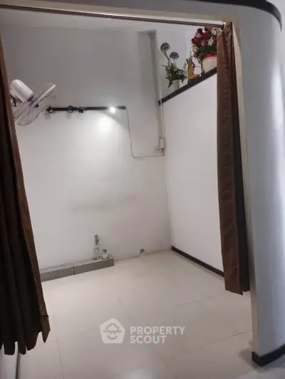 Minimalist interior space with white walls and tiled floor, featuring a wall-mounted fan and decorative plants.