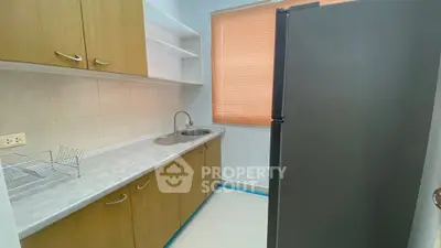 Compact kitchen with modern fridge and wooden cabinets, perfect for efficient cooking.