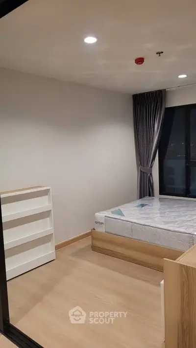 Modern bedroom with wooden flooring and large window, featuring a minimalist design and ample natural light.