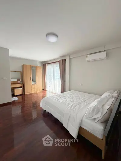 Spacious bedroom with wooden flooring and natural light, featuring a cozy bed and modern wardrobe.
