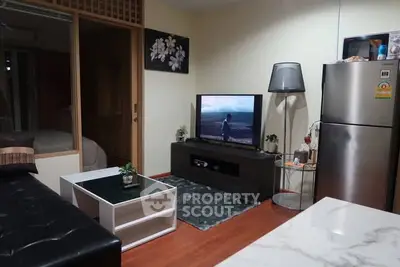 Cozy living room with modern decor and TV, adjacent to a compact kitchen area.