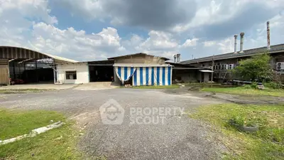 Industrial warehouse exterior with spacious parking area under a cloudy sky.