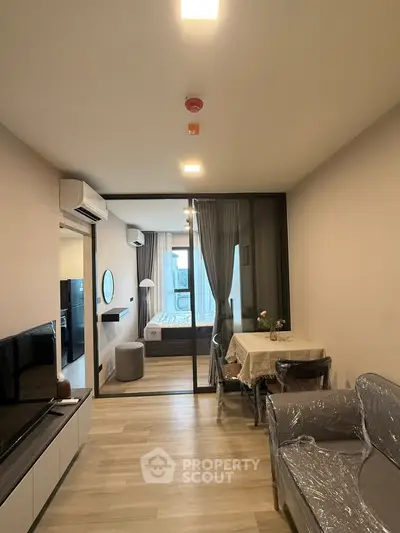 Modern apartment interior with open living and dining area leading to a cozy bedroom.