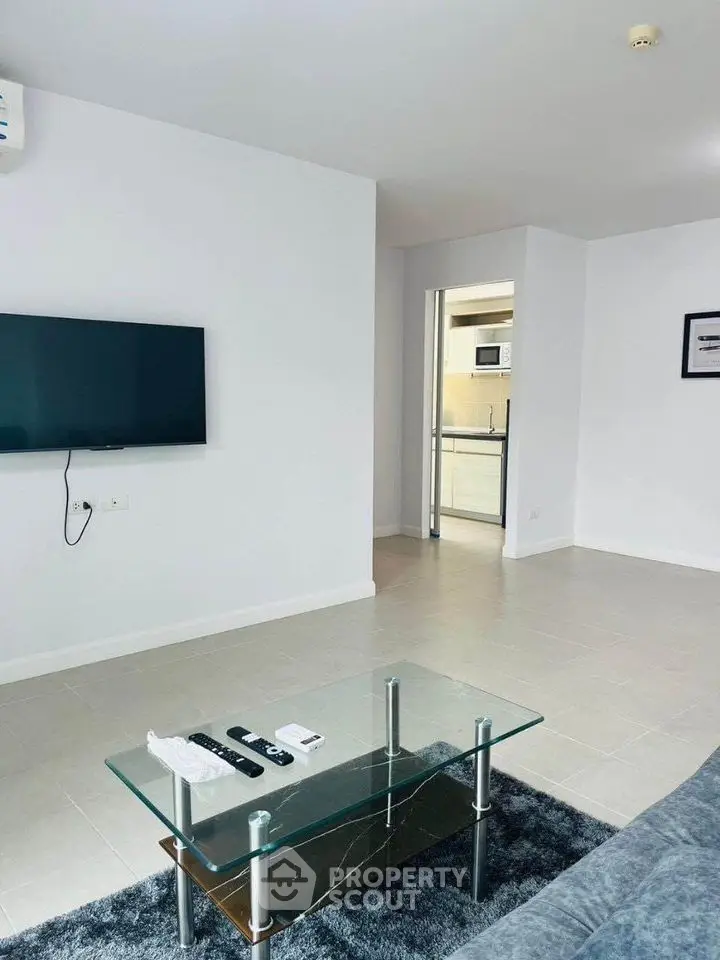Modern living room with wall-mounted TV and glass coffee table in a sleek apartment.