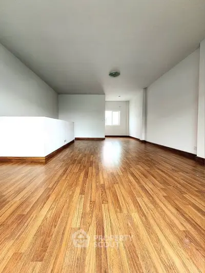 Spacious empty room with wooden flooring and white walls, ideal for customization.