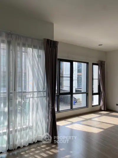 Spacious sunlit living room with large windows and elegant curtains