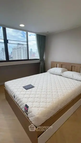 Modern bedroom with large window and city view, featuring a comfortable bed and stylish decor.