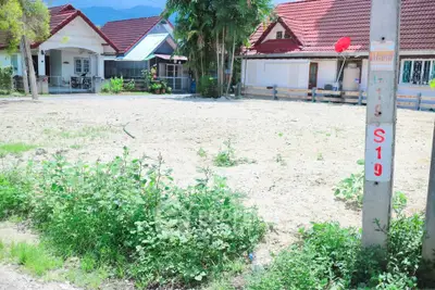 Vacant land plot in a residential area with nearby houses and lush greenery.