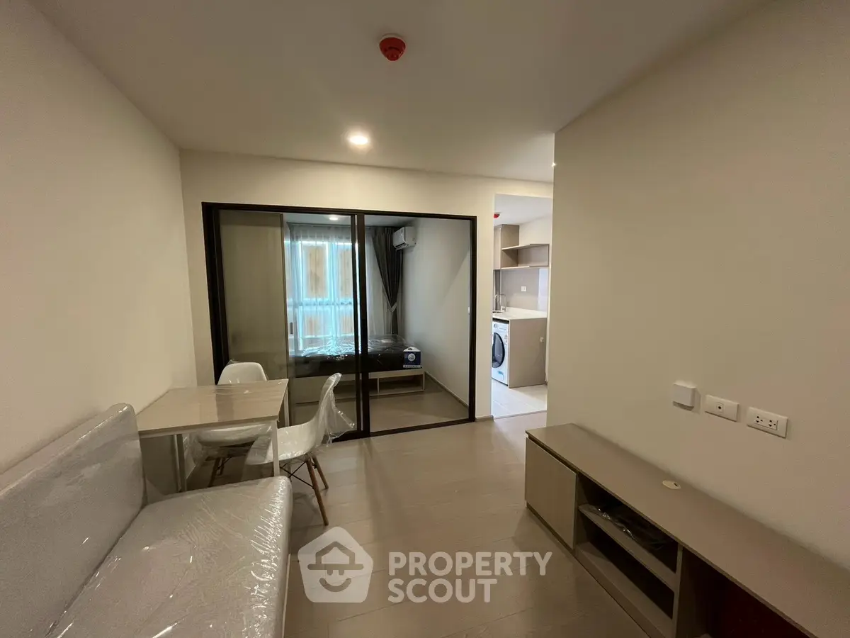 Modern apartment interior with open living area and bedroom, featuring sleek furniture and natural light.
