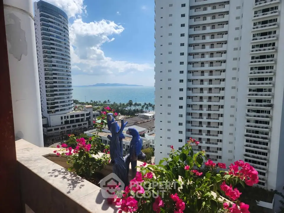 Stunning ocean view from high-rise balcony with vibrant flowers and cityscape.