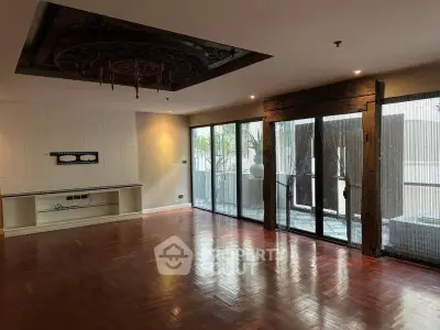 Spacious living room with wooden flooring and large windows opening to a balcony.