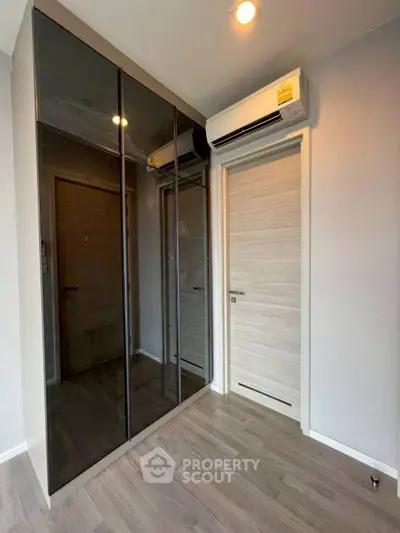 Modern bedroom with sleek mirrored wardrobe and air conditioning unit.