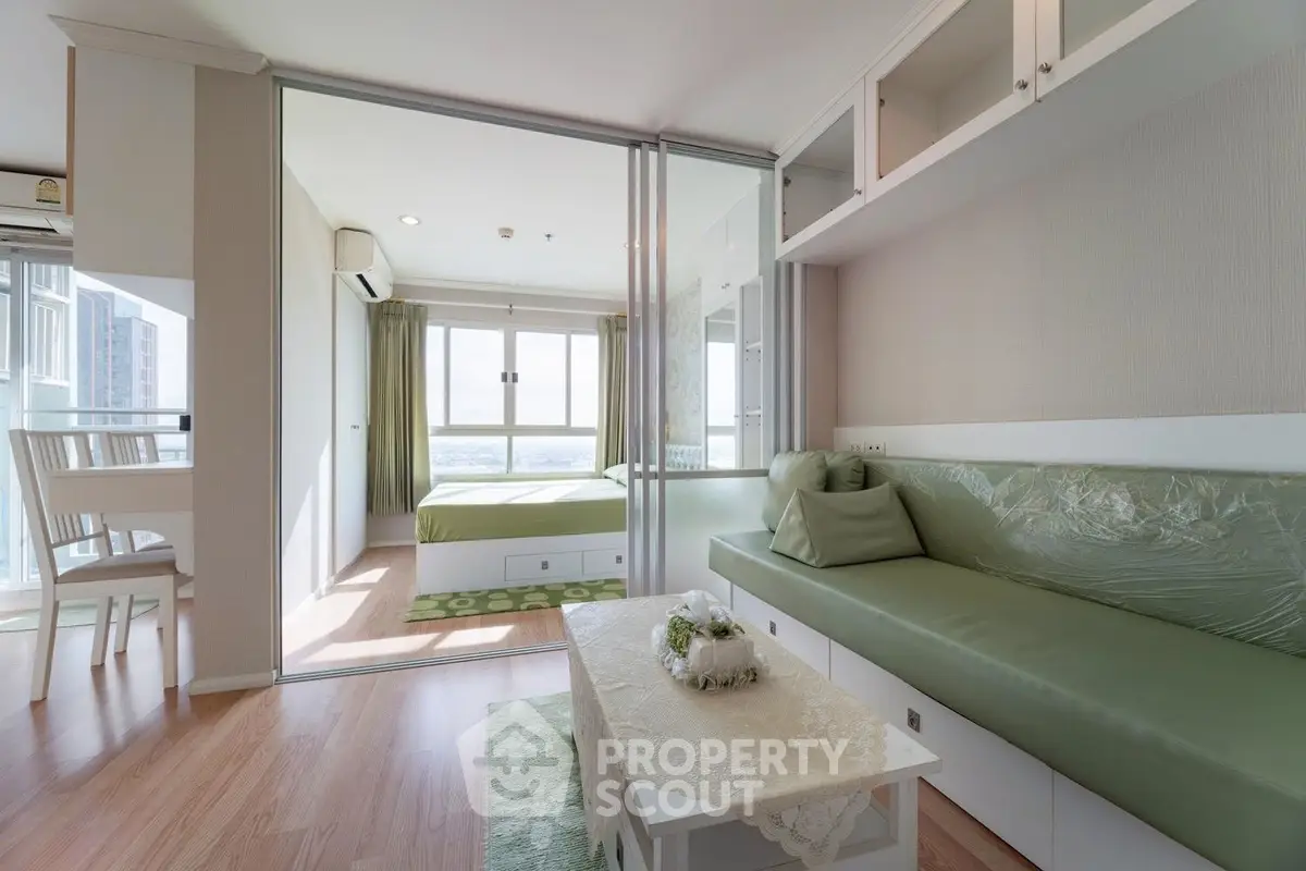 Modern living room with green sofa and glass partition leading to a bright bedroom.