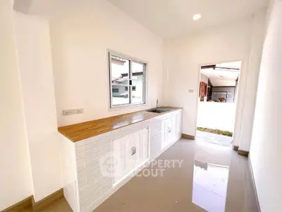 Bright kitchen with sleek white cabinetry and wooden countertop, featuring a window view and glossy tiled floor.