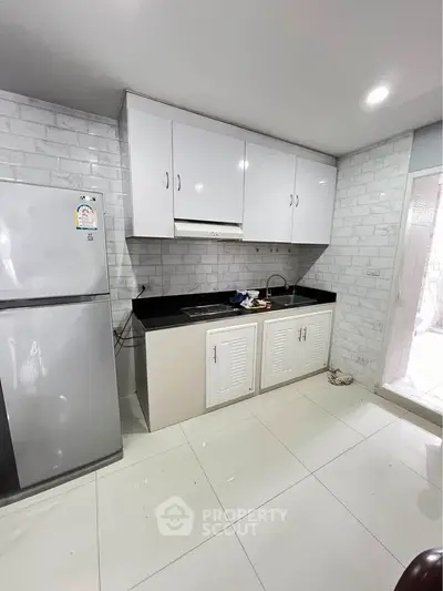Modern kitchen with sleek white cabinets and stainless steel fridge in a stylish apartment.