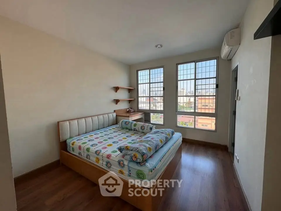Cozy bedroom with large windows and wooden flooring, featuring a comfortable bed and air conditioning.