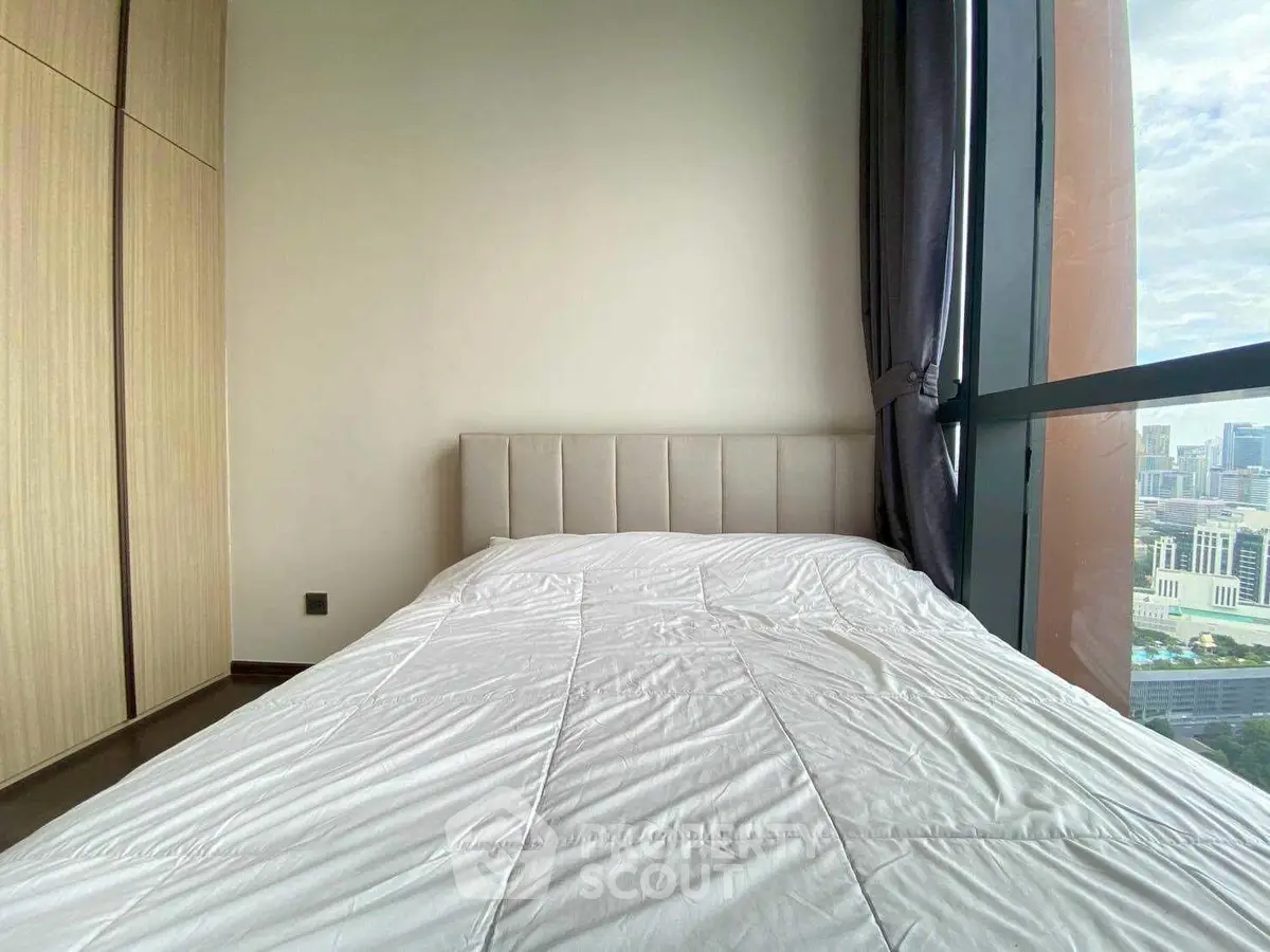 Modern bedroom with city view and large window, featuring a cozy bed and built-in wardrobe.