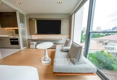 Modern living room with large windows and city view, featuring sleek furniture and open kitchen layout.