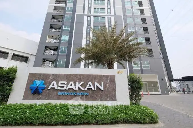 Modern apartment building with Asakan Srinakarin sign and palm tree landscaping.