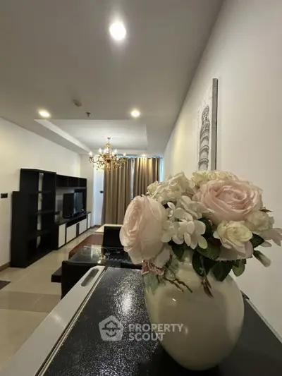 Elegant living room with modern decor and floral centerpiece, featuring a cozy seating area and stylish chandelier.