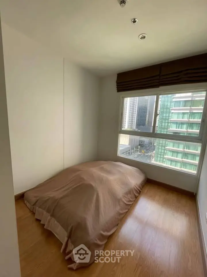 Cozy bedroom with large window offering city view, featuring minimalist decor and wooden flooring.