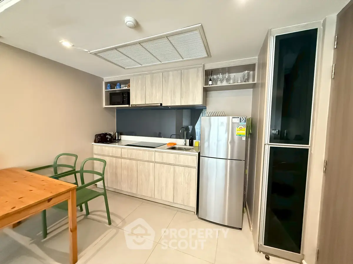 Modern kitchen with sleek cabinets, stainless steel fridge, and dining area in stylish apartment.