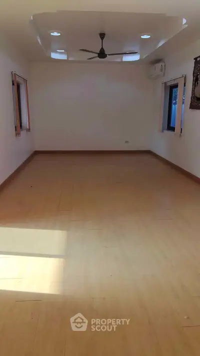 Spacious empty room with wooden flooring and ceiling fan, ideal for customization.