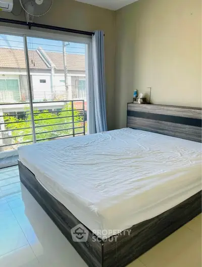 Spacious bedroom with large window and modern bed frame, offering natural light and a serene view.