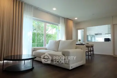 Spacious modern living room with large windows and open kitchen layout, featuring elegant furnishings.