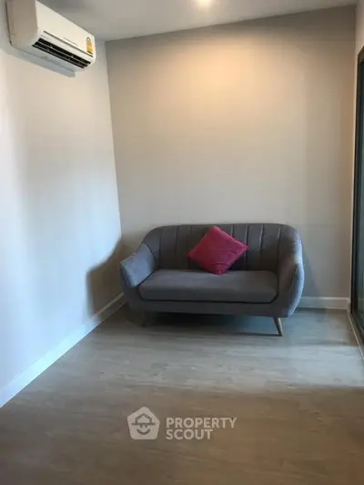 Cozy minimalist living room with modern gray sofa and red accent pillow, featuring sleek wooden flooring.
