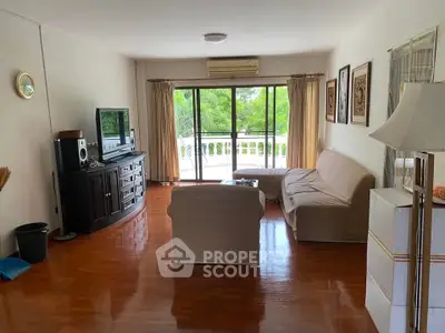 Spacious living room with large windows and balcony view, featuring cozy seating and entertainment center.