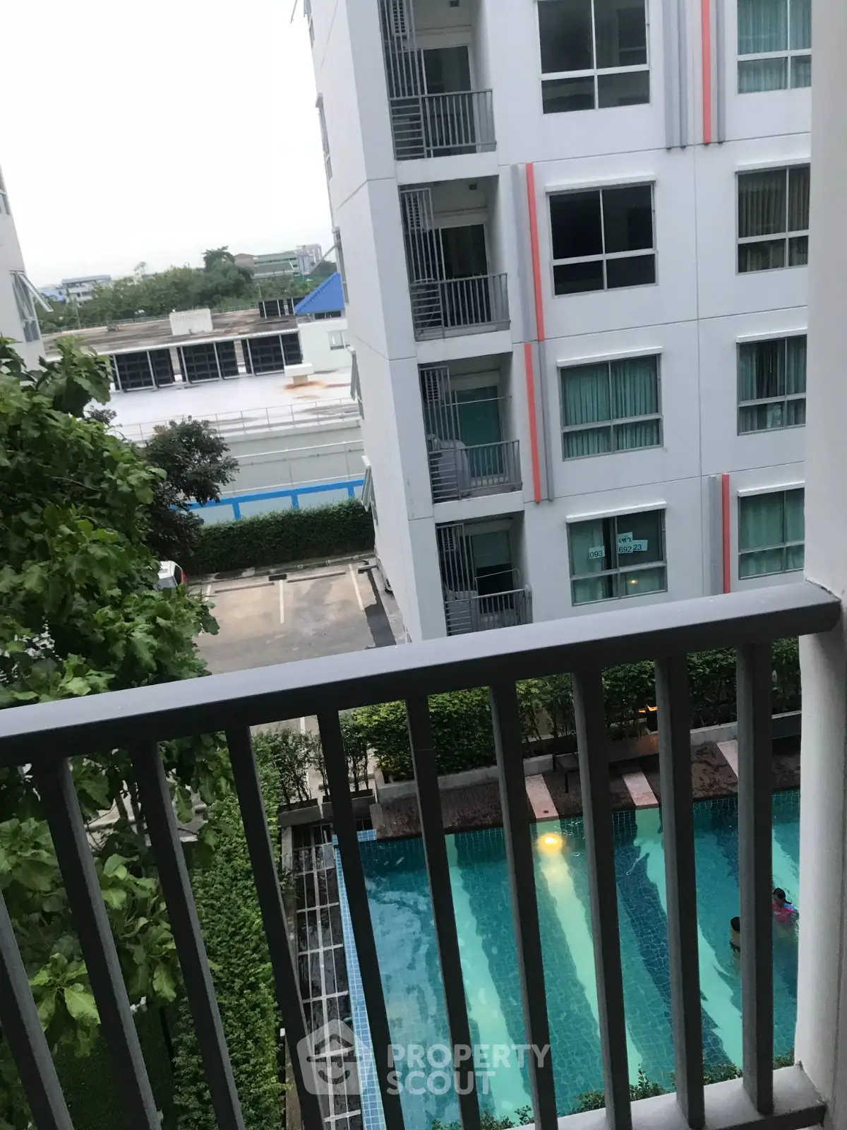 Modern apartment view with pool and balcony overlooking lush greenery and urban surroundings.