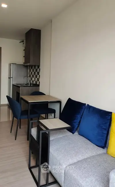 Modern living room with stylish furniture and compact kitchen area in open layout apartment.