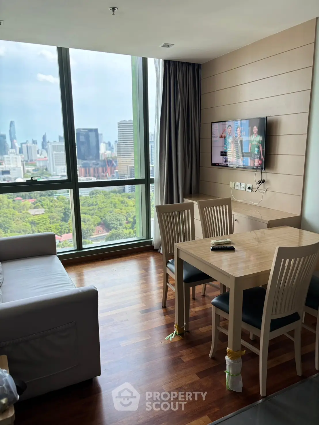 Modern living room with stunning city view, wooden flooring, and wall-mounted TV in a high-rise apartment.