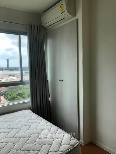 Cozy bedroom with large window and built-in wardrobe offering city views.