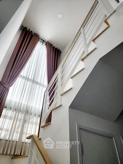 Modern staircase with tall windows and elegant curtains in a stylish home interior.