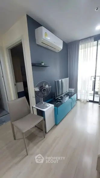 Modern living room with sleek furniture and natural light, featuring a TV and air conditioning.