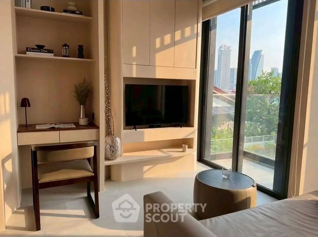 Modern living room with large windows and city view, featuring built-in shelves and a cozy workspace.