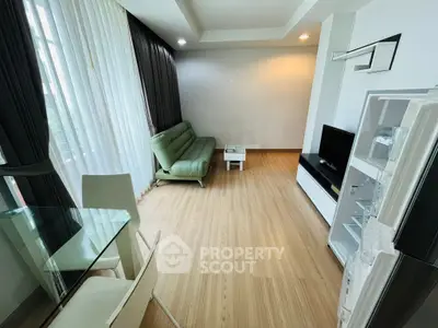 Modern living room with sleek furniture and natural light, featuring a green sofa and flat-screen TV.
