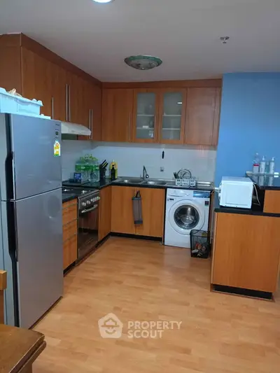 Modern kitchen with wooden cabinets, stainless steel appliances, and washing machine.