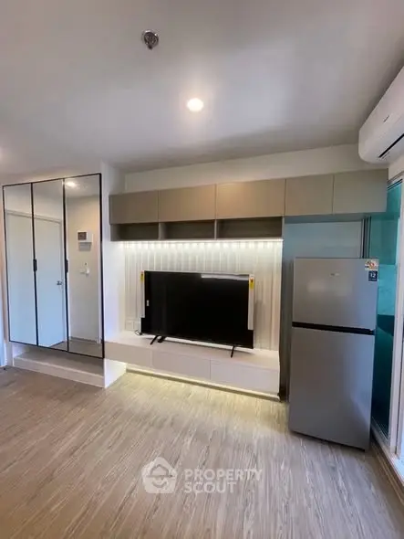 Modern living room with sleek TV unit and stainless steel fridge, showcasing contemporary design.