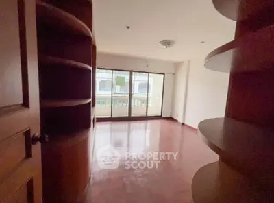 Spacious living room with wooden floors and large windows leading to a balcony.