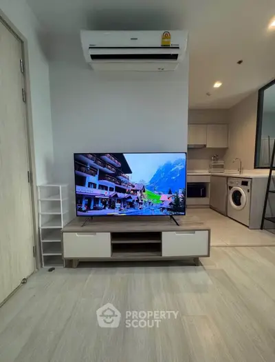 Modern living room with TV, air conditioning, and open kitchen layout featuring washing machine.