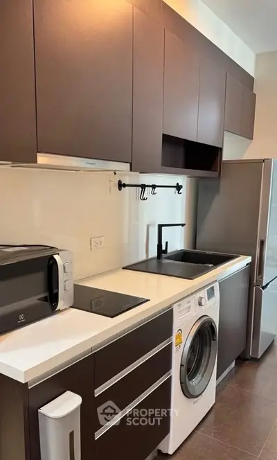 Modern kitchen with sleek cabinets, washing machine, and stainless steel appliances.