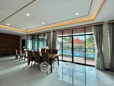 Spacious dining area with large windows overlooking a pool and garden, featuring elegant furniture and modern lighting.