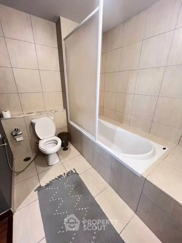 Modern bathroom with bathtub and tiled walls, featuring a sleek design and neutral tones.