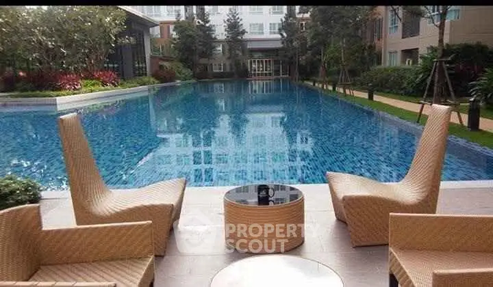 Luxurious poolside area with modern wicker chairs and lush landscaping in a high-end residential complex.