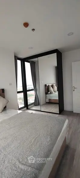 Modern bedroom with large mirrored wardrobe and city view window.